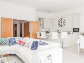 A white sectional sofa with fish and union jack pillows in an open plan kitchen and dining area with bar stools and a large wall clock at Bay Sea View in Torquay