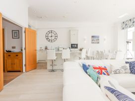 A white living room and kitchen area with bar stools and colorful cushions on a sofa at Bay Sea View in Torquay
