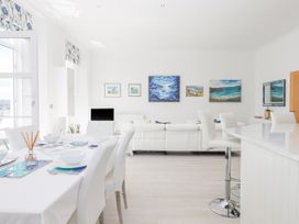 A white dining table set with bowls glasses and placemats next to a white sofa and kitchen island with bar stools in a living room at Bay Sea View in Torquay