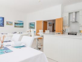 A dining table set with plates and bowls next to a kitchen island with stools and a living room with paintings on walls at Bay Sea View in Torquay