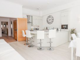 A kitchen with white cabinets a white island with four white bar stools a wall clock and a wooden door at Bay Sea View in Torquay