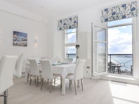 A dining room with a table set for meals and a door open to a balcony overlooking water at Bay Sea View in Torquay