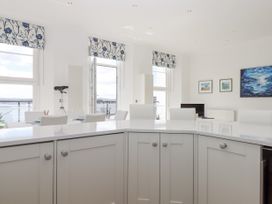 A modern kitchen with white cabinets and a countertop overlooking a dining area with white chairs and large windows at Bay Sea View in Torquay