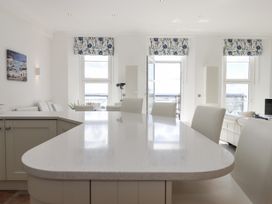 A kitchen island with white chairs and windows with floral curtains at Bay Sea View in Torquay