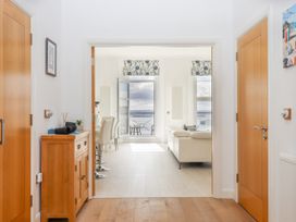 A hallway with wooden floor and cabinet leading to a living room with dining chairs white sofa and sea view at Bay Sea View in Torquay