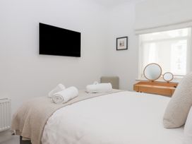 A bedroom with a bed and rolled towels on a blanket a mounted tv a small framed picture and a wooden vanity with mirrors at Bay Sea View in Torquay