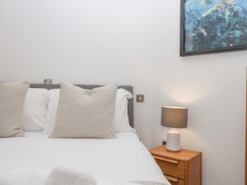 A bed with white sheets and beige pillows next to a wooden nightstand with a lamp and a framed painting on the wall at Bay Sea View in Torquay