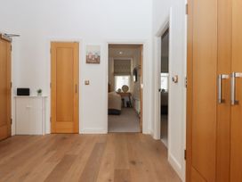 A hallway with wooden flooring two wooden doors and a white small cabinet with a plant and speaker on top at Bay Sea View in Torquay