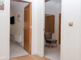 A hallway with two open doors showing a room with a wall-mounted TV and radiator and another room with a chair and mirror at Bay Sea View in Torquay