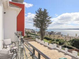 A balcony with two chairs and a table overlooking a courtyard garden and sea with buildings in the background at Bay Sea View in Torquay
