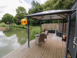 A patio area with chairs and a table near a pond at Maple Lodge at Bridge Lake Farm & Fishery Chacombe