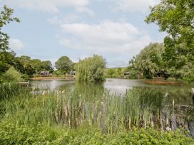A view of a lake surrounded by trees and houses at Maple Lodge at Bridge Lake Farm & Fishery Chacombe
