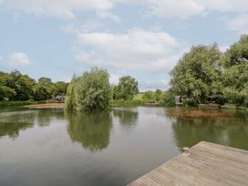 View of a lake with trees and fishing huts at Maple Lodge at Bridge Lake Farm & Fishery, Chacombe