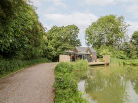 A cabin by a lake surrounded by trees at Maple Lodge at Bridge Lake Farm & Fishery Chacombe
