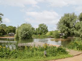 A pond surrounded by trees and benches at Maple Lodge at Bridge Lake Farm & Fishery, Chacombe