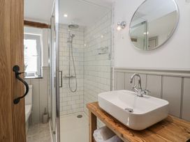 A bathroom with a wooden door a shower with white tiled walls a sink on a wooden counter and a round mirror at Style Cottage in Keswick