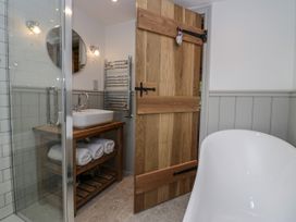 A bathroom with a wooden door a white bathtub a sink on a wooden stand with towels and a glass shower at Style Cottage in Keswick