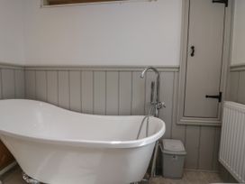 A bathroom with a white freestanding bathtub and a small cabinet on a gray paneled wall at Style Cottage in Keswick