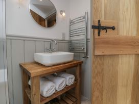 A bathroom with a wooden sink vanity holding a white basin and towels under it at Style Cottage in Keswick