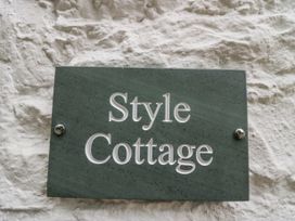A green plaque with Style Cottage text on a white textured wall at Style Cottage in Keswick