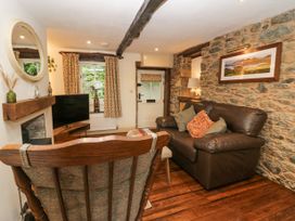 A living room with a brown leather sofa wooden chair stone wall and a television at Style Cottage in Keswick
