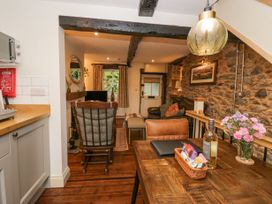 A dining area with a wooden table, chair, flowers, and snacks next to a living room with a rocking chair, couch, and stone wall at Style Cottage in Keswick