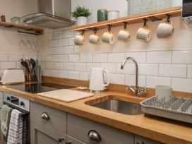 A kitchen counter with a sink a kettle hanging mugs and utensils at Style Cottage in Keswick
