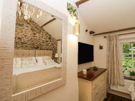 A bedroom with a stone wall bed reflected in a mirror and a dresser with a TV above it at Style Cottage in Keswick