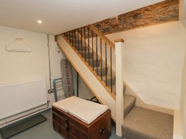 A staircase with carpeted steps and wooden handrails with metal balusters and a wooden chest with cushions underneath the stairs at Style Cottage in Keswick