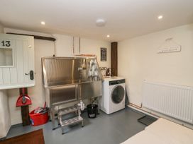 A utility room with a stainless steel wash basin, washing machine, red bucket, and cleaning tools at Style Cottage in Keswick