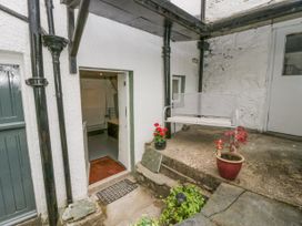 A small outdoor patio area with a white bench two potted plants and an open doorway leading inside at Style Cottage in Keswick