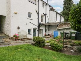 An outdoor garden area with green grass bushes potted flowers and white building with doors and windows at Style Cottage in Keswick