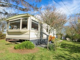 A mobile home with a porch and garden chairs on grass surrounded by trees at Fron Dderw Caravan in Llanfairynghornwy near Llanfechell