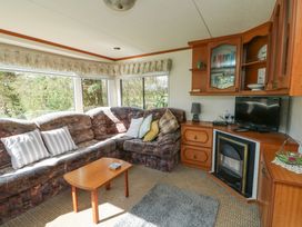 A living room with a patterned corner sofa, wooden coffee table, built-in wooden cabinets, a television, and a fireplace at Fron Dderw Caravan in Llanfairynghornwy near Llanfechell