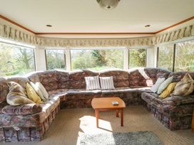 A living area with a large patterned corner sofa with cushions and a wooden coffee table in front of windows at Fron Dderw Caravan in Llanfairynghornwy near Llanfechell