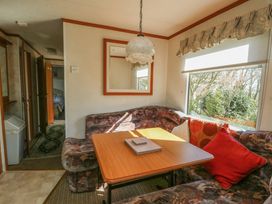 A dining area with a wooden table and cushioned seating near a window with curtains in Fron Dderw Caravan Llanfairynghornwy near Llanfechell
