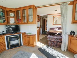 An interior living area with wooden cabinets a television a fireplace a patterned sofa and a dining table with seating at Fron Dderw Caravan Llanfairynghornwy near Llanfechell