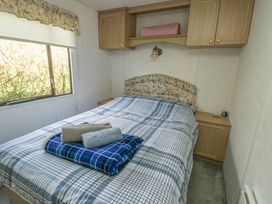 A bedroom with a double bed and blue plaid bedding next to a window with floral valance at Fron Dderw Caravan Llanfairynghornwy near Llanfechell