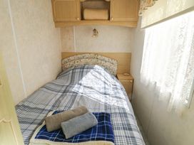 A small bedroom with a single bed covered in a plaid blanket and towels on top a bedside table and window with lace curtains at Fron Dderw Caravan Llanfairynghornwy near Llanfechell