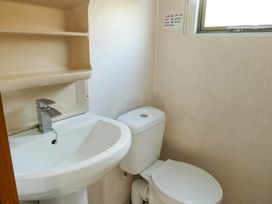 A small bathroom with a white sink and faucet and a white toilet near a window at Fron Dderw Caravan Llanfairynghornwy near Llanfechell