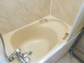 A beige bathtub with chrome faucet and handheld shower in a bathroom at Fron Dderw Caravan in Llanfairynghornwy near Llanfechell