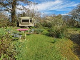A garden with metal chairs and a round table near a caravan by a pond at Fron Dderw Caravan Llanfairynghornwy near Llanfechell