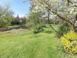 A garden with grass trees shrubs and a pond at Fron Dderw Caravan in Llanfairynghornwy near Llanfechell