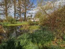 A pond surrounded by plants and trees with a caravan and outdoor table and chairs at Fron Dderw Caravan Llanfairynghornwy near Llanfechell