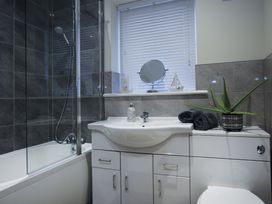 A bathroom with a shower, bathtub, vanity, mirror, and plant at Apartment 3 in Trearddur Bay