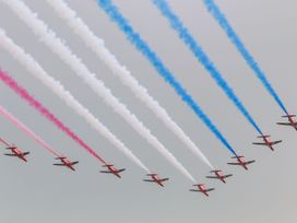 Nine red planes flying in formation leaving red white and blue smoke trails in the sky