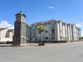 A stone clock tower next to a three-story residential building on a clear day at Escape To The Chapel Anglesey Bryngwran near Rhosneigr