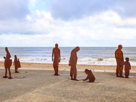 Rust-colored metal statues of people on a beach promenade near the ocean at The Old Post Office in Llanelian near Old Colwyn
