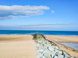 A sandy beach with a rock jetty leading to the sea and wind turbines on the horizon at The Old Post Office in Llanelian near Old Colwyn