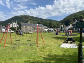 An outdoor play area with swings and playground equipment at Swn Yr Afon in Abergynolwyn near Tywyn